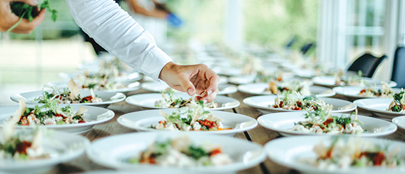 a caterer garnishing a number of dishes with herbs for a wedding reception