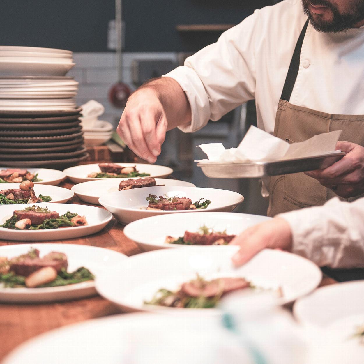 a chef sprinkling herbs on a number of plates for a catered event